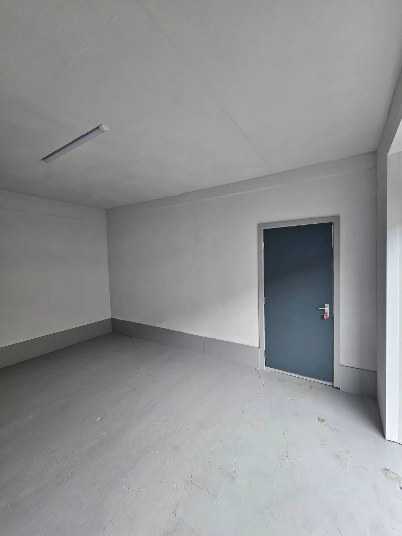Inside the 150 sq ft unit: grey painted floor, white walls, overhead light and a dark grey door