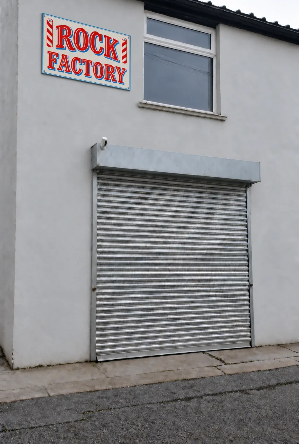 Outside the two-storey unit: Rock Factory sign, first-floor window and a galvanised roller shutter with a security camera above