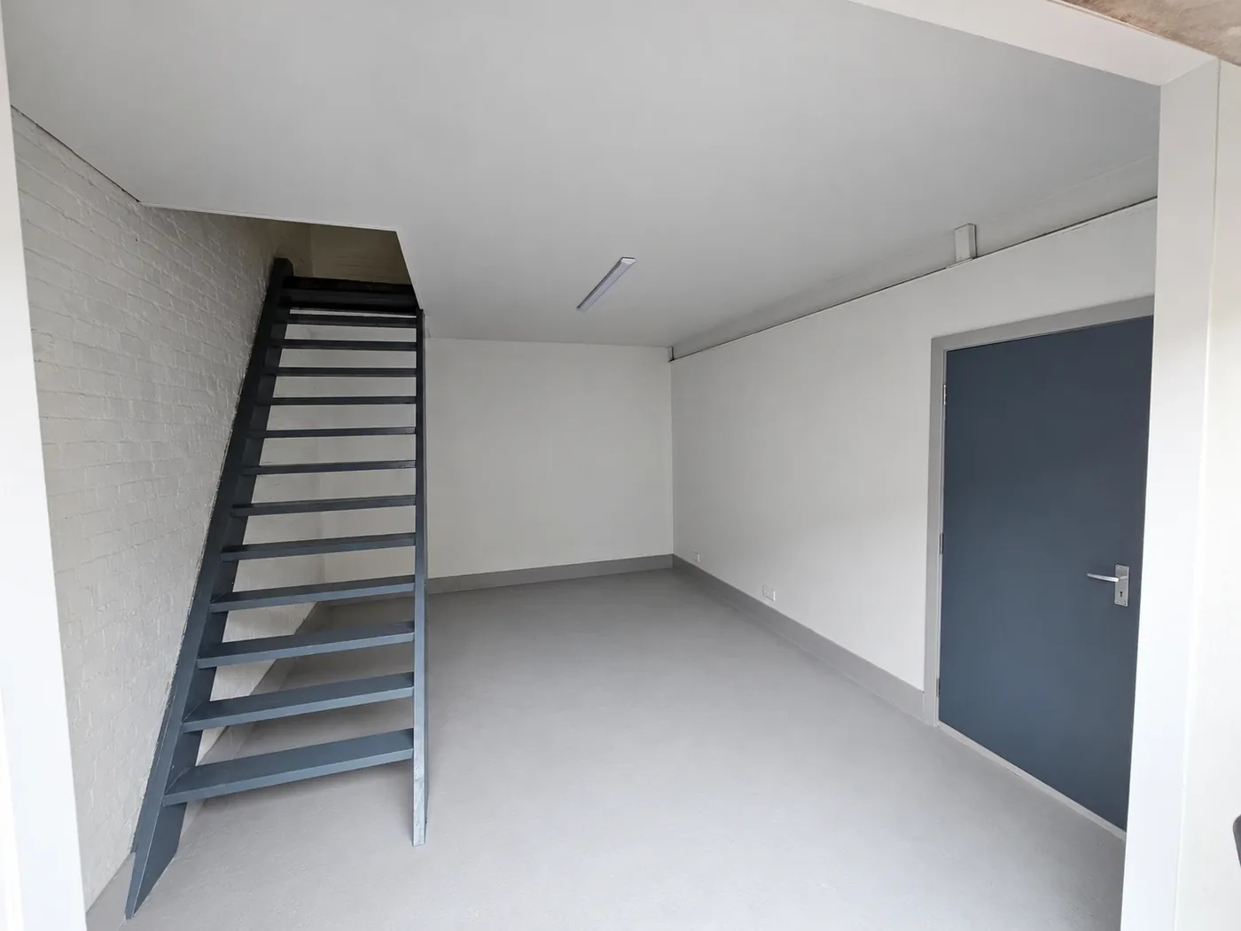 Inside the 300 sq ft two-storey unit: grey floor, white walls, a dark grey staircase up to the first floor and a grey door